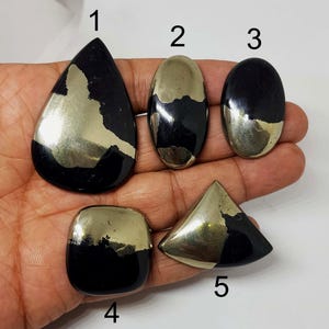 Pode incluir: Cinco pedras preciosas de pirita polidas em várias formas: gota, oval, quadrada e triangular. Cada pedra tem uma seção dourada metálica brilhante e uma seção preta brilhante. As pedras preciosas são exibidas em um fundo claro.