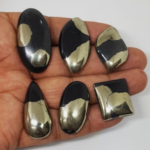 Pode incluir: Seis pedras preciosas de pirite polidas em várias formas, incluindo oval, gota e quadrada. As pedras têm uma superfície escura e brilhante com inclusões metálicas douradas, criando um contraste marcante. As pedras preciosas são exibidas em um fundo neutro.