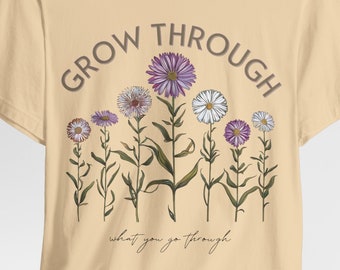 Puede incluir: Una camiseta beige con un diseño floral y el texto "GROW THROUGH what you go through".