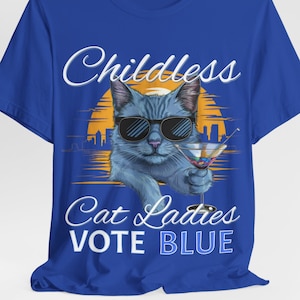 May include: Blue t-shirt with a graphic of a cat wearing sunglasses and holding a martini glass. The text "Childless Cat Ladies Vote Blue" is printed on the shirt.