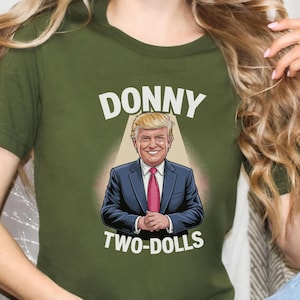 May include: A green t-shirt with a cartoon image of Donald Trump in a suit and tie. The text "Donny Two-Dolls" is printed below the image.