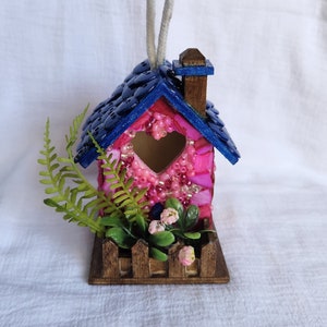 Hanging birdhouse, its roof is decorated with blue buttons, and walls with colorful pink shells and glass beads.