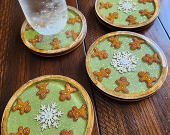 Peut inclure: Quatre dessous de verre ronds avec un fond vert, des paillettes et des bonhommes en pain d'épices. Chaque dessous de verre a une bordure en bois et un dessus transparent. Un verre d'eau repose sur l'un des dessous de verre.