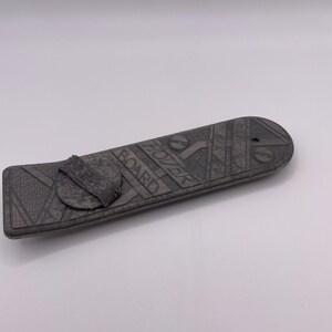 Puede incluir: Una tabla de skate gris con un patrón geométrico blanco y negro y las palabras "The Board" impresas en ella.