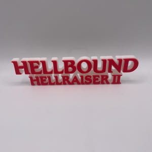 Peut inclure: Un panneau imprimé en 3D blanc et rouge avec le texte "HELLBOUND" en grandes lettres en gras, et "HELLRAISER II" en plus petites lettres en dessous. Ce panneau est probablement un objet décoratif ou de collection.