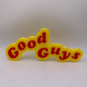 Peut inclure: Une enseigne en plastique jaune avec les mots "Good Guys" en lettres rouges.