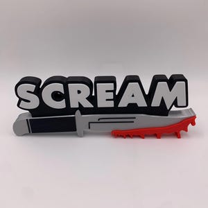 May include: A black and white 3D printed sign that says "SCREAM" with a silver knife and red dripping blood.