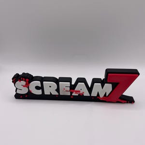 May include: A black and white "SCREAM 7" logo with red accents. The word "SCREAM" is in white block letters with red blood splatter details. The number "7" is in red, with a black outline.