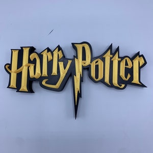 May include: A 3D printed Harry Potter logo with a black outline and gold fill. The logo features the iconic lightning bolt.