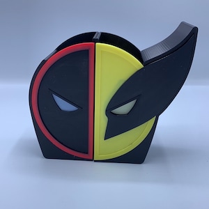 May include: A black and yellow 3D printed desk organizer shaped like the heads of Deadpool and Wolverine. The organizer has two compartments for holding pens, pencils, or other office supplies.