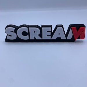 Puede incluir: Un letrero impreso en 3D en blanco y negro con la palabra "SCREAM" en letras blancas y una "V" roja al final.