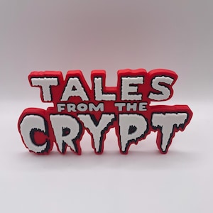 Può includere: Un cartello rosso e bianco con la scritta "TALES FROM THE CRYPT". Il cartello ha un effetto 3D con lettere bianche e un contorno rosso. Il testo è in un carattere in grassetto e stilizzato.