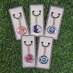 May include: Five keychains with circular pendants in various colors, each attached to a silver chain and a key ring. The pendants feature different geometric designs and are displayed on cardboard packaging. The text "Beast Yeast Keychain" is printed on the packaging.