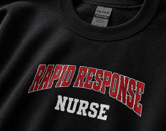 May include: A black crewneck sweatshirt featuring the text RAPID RESPONSE in a red arched font with a white outline, and the word NURSE in a white block font underneath. The interior collar tag displays the Gildan Heavy Blend brand logo.