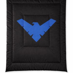 Może przedstawiać: Czarna kołdra z dużym niebieskim emblematem ptaka. Emblemat jest wyśrodkowany na kołdrze, kt&oacute;ra ma pikowany wz&oacute;r. Kołdra jest w jednolitym czarnym kolorze.