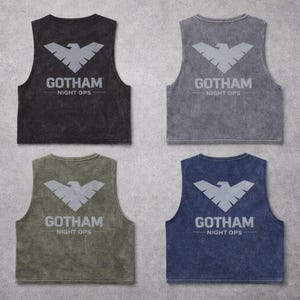 May include: Four sleeveless tank tops in black, gray, olive green, and navy blue. Each tank top features a gray bat symbol and the text "GOTHAM NIGHT OPS" printed on the back. The tops have a vintage, washed appearance.