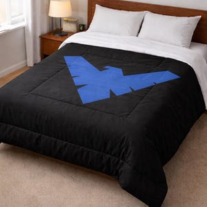 Może przedstawiać: Czarna kołdra z dużym niebieskim geometrycznym wzorem. Ł&oacute;żko jest pościelone białymi prześcieradłami i poduszkami. Kołdra leży na drewnianej ramie ł&oacute;żka. Lampa i stolik nocny są widoczne w tle.