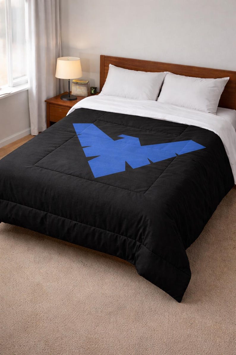 Może przedstawiać: Czarna kołdra z dużym niebieskim geometrycznym wzorem. Ł&oacute;żko jest pościelone białymi prześcieradłami i poduszkami. Kołdra leży na drewnianej ramie ł&oacute;żka. Lampa i stolik nocny są widoczne w tle.