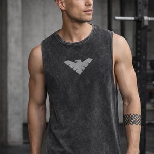 May include: Dark gray sleeveless workout shirt with a faded texture and a gray eagle logo on the chest. The shirt is made of a soft material and is suitable for gym or casual wear.