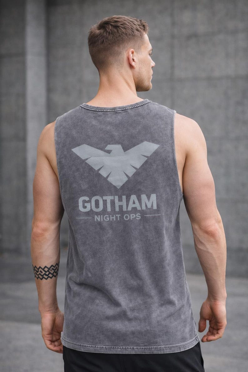 May include: Gray tank top with the text "GOTHAM NIGHT OPS" and a stylized bird emblem on the back. The sleeveless shirt is made of a soft, textured fabric.