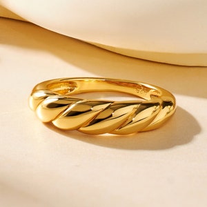 May include: A gold-toned ring with a thick, twisted band. The ring is made of metal and has a smooth, polished finish.