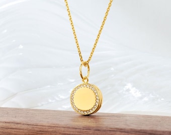 Può includere: Una collana d'oro con un ciondolo rotondo con un cerchio di piccoli diamanti attorno al bordo.