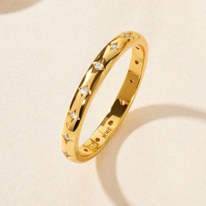 May include: A gold band ring with a row of small diamonds set in a starburst pattern. The ring is engraved with the word "J.ORE."
