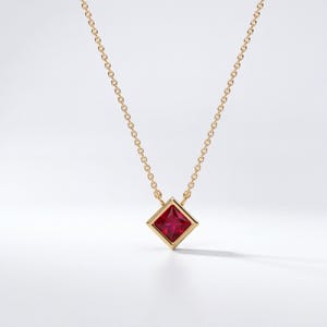 May include: A gold chain necklace featuring a single square-cut red gemstone pendant set in a gold bezel. The pendant is suspended from a delicate gold link chain, showcasing a vibrant crimson stone with a faceted surface and a polished gold frame.