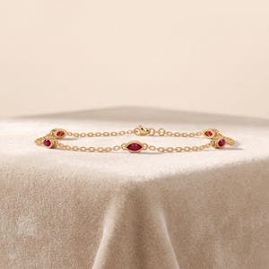 May include: A delicate gold chain bracelet featuring four evenly spaced marquise-cut red rubies set in gold bezels. The bracelet is constructed with fine oval links and includes a small lobster claw clasp closure at the back of the chain.