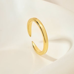 Könnte beinhalten: Ein einfacher, verstellbarer Goldring mit einem glatten, abgerundeten Band. Der Ring ist an einer Seite offen, so dass er an verschiedene Fingergrößen angepasst werden kann.