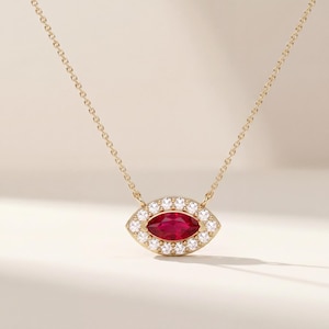 May include: A gold chain necklace featuring a central pendant shaped like an eye. The pendant contains a marquise-cut red ruby gemstone at the center, surrounded by a halo of small, round, clear white diamonds set in a gold frame.