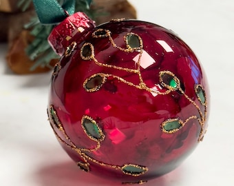 May include: A red glass Christmas ornament with gold and green leaf designs.