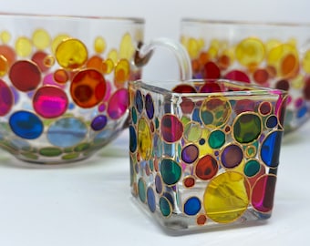 Pode incluir: Conjunto de três copos de vidro com círculos coloridos delineados em ouro. Os copos são transparentes e os círculos são pintados no exterior.
