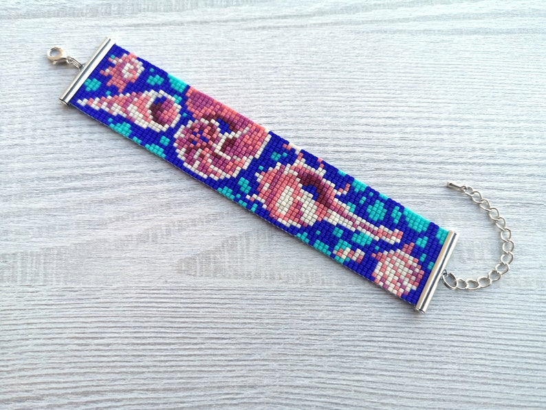 May include: A beaded bracelet with a colorful pattern of pink, blue, and white beads. The bracelet has a silver clasp and chain.
