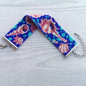 May include: A beaded bracelet with a colorful geometric pattern in shades of pink, blue, and white. The bracelet has silver metal clasps.