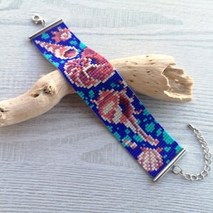 May include: A beaded bracelet with a colorful design of seashells and coral on a blue background. The bracelet has silver clasps.