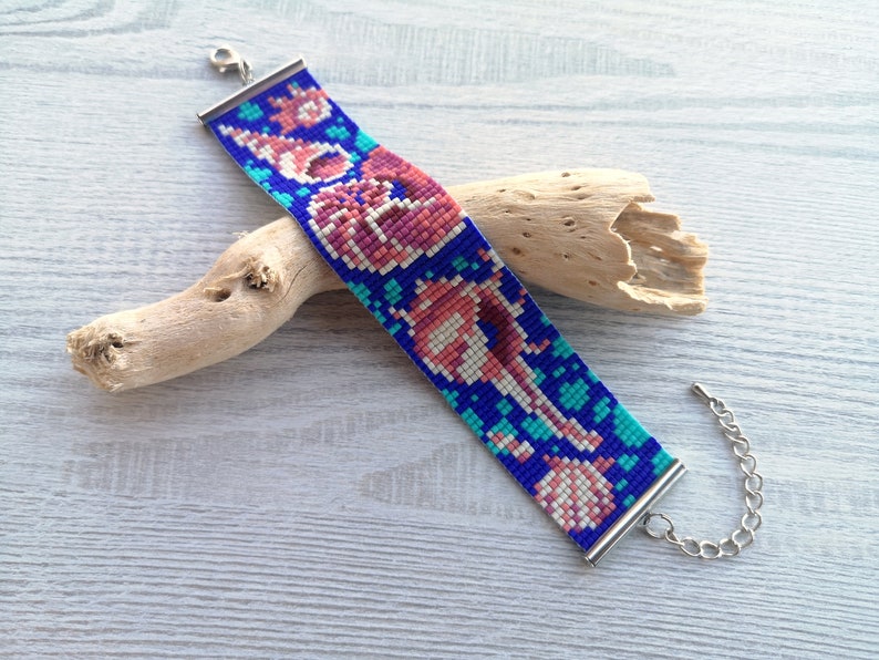 May include: A beaded bracelet with a colorful design of seashells and coral on a blue background. The bracelet has silver clasps.