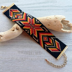 May include: A black beaded bracelet with a geometric pattern in orange, red, and gold. The bracelet has a gold clasp.
