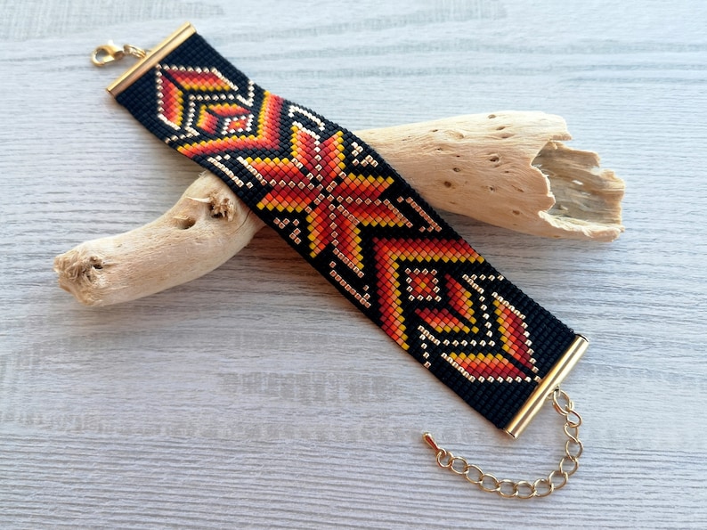 May include: A black beaded bracelet with a geometric pattern in orange, red, and gold. The bracelet has a gold clasp.