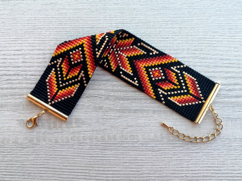 May include: A black beaded bracelet with a geometric pattern in orange, red, and gold. The bracelet has a gold clasp and chain.