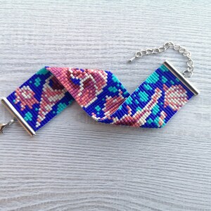 May include: A beaded bracelet with a blue, pink, and white geometric pattern. The bracelet has a silver clasp and chain.