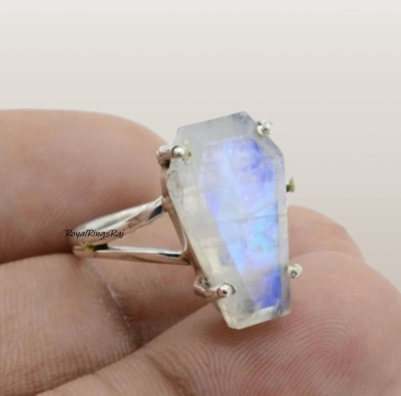 May include: A coffin-shaped moonstone ring with a silver band. The moonstone has a translucent, iridescent quality with blue and white hues. The ring's design is unique and eye-catching, perfect for those who appreciate alternative jewelry.