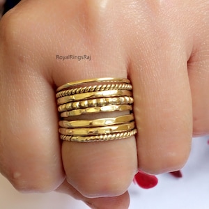 Peut inclure: Un ensemble de neuf bagues empilables en or, présentant une variété de textures et de styles, notamment martelées, perlées et torsadées. Les bagues sont portées sur un doigt.