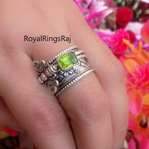 May include: A silver ring with a rectangular, light green gemstone. The ring features a bee design on one side and floral patterns. The text "RoyalRingsRaj" is visible.