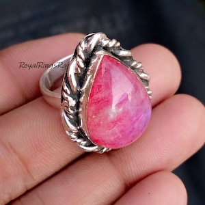 Op de afbeelding: Een zilveren ring met een grote, druppelvormige roze edelsteen. De edelsteen is gezet in een decoratieve, getextureerde zilveren bezel. De ring wordt in een hand gehouden, met de tekst "RoyalRingsRaj" zichtbaar.