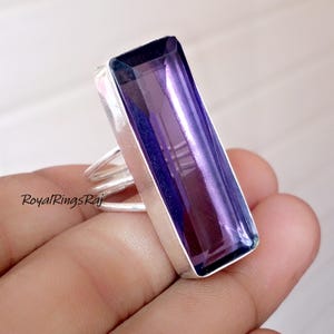 May include: A rectangular amethyst gemstone ring with a silver band. The gemstone is a deep purple color and is set in a silver bezel. The ring has a simple, elegant design.