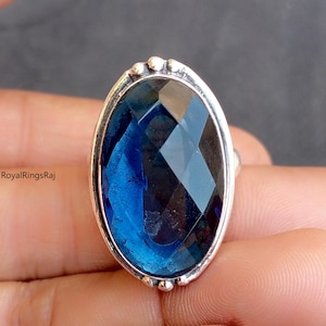 Op de afbeelding: Een zilveren ring met een grote, ovale, gefacetteerde blauwe edelsteen.