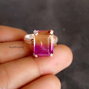 Puede incluir: Un anillo de plata con una gran gema rectangular. La piedra muestra un degradado de color, pasando de un naranja-amarillo cálido en la parte superior a un magenta-púrpura vibrante en la parte inferior. La banda del anillo es de plata pulida.