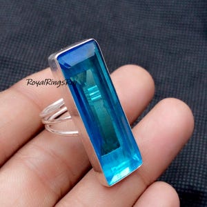 Op de afbeelding: Een rechthoekige blauwe edelsteenring met een zilveren band. De edelsteen heeft een levendige blauwe kleur en is gezet in een zilveren bezel. De ring heeft een eenvoudig, elegant ontwerp.