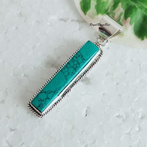 Könnte beinhalten: Ein Anhänger aus türkisfarbenem Stein mit einer silbernen Fassung. Der Stein ist rechteckig und hat eine strukturierte Oberfläche. Der Anhänger befindet sich auf einem weißen Hintergrund.